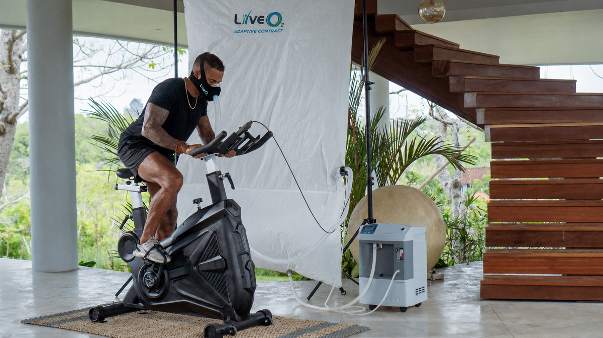 LiveO2 Adaptive Contrast EWOT system with extra-large high altitude chamber and athlete using oxygen mask on an exercise bike in a covered training space