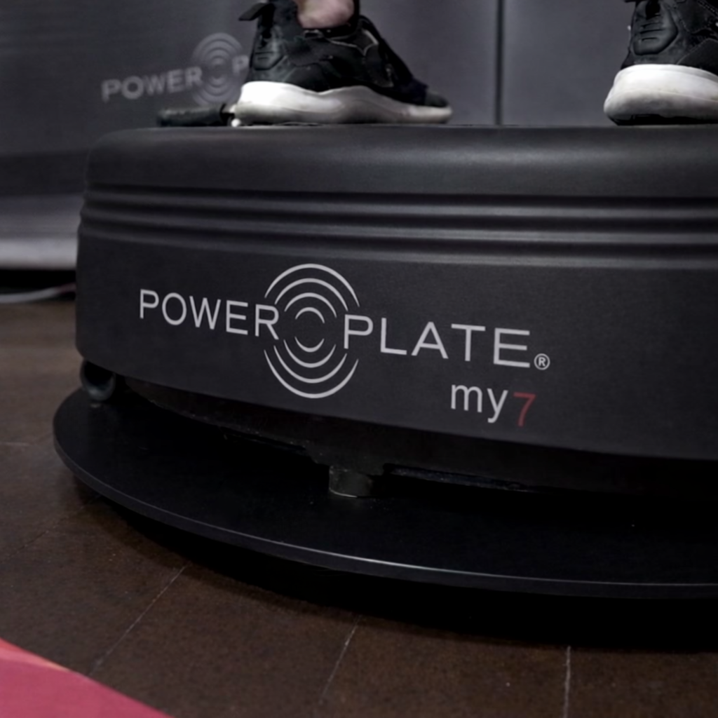 Power Plate my7 vibration system placed on Power Shield base reducing vibration transfer on hardwood floor with training mat visible in foreground within home or studio environment