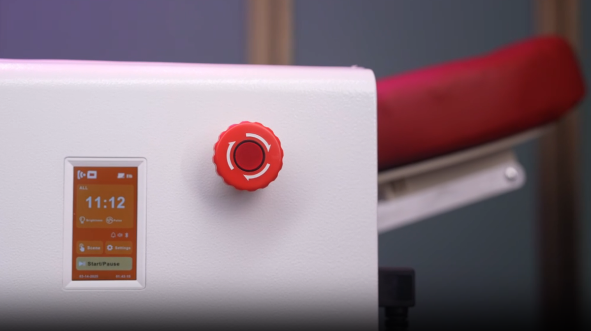 Prestige Pro Modular Red Light Therapy Bed touchscreen control panel and emergency stop button shown in close-up with adjustable headrest visible in the background.
