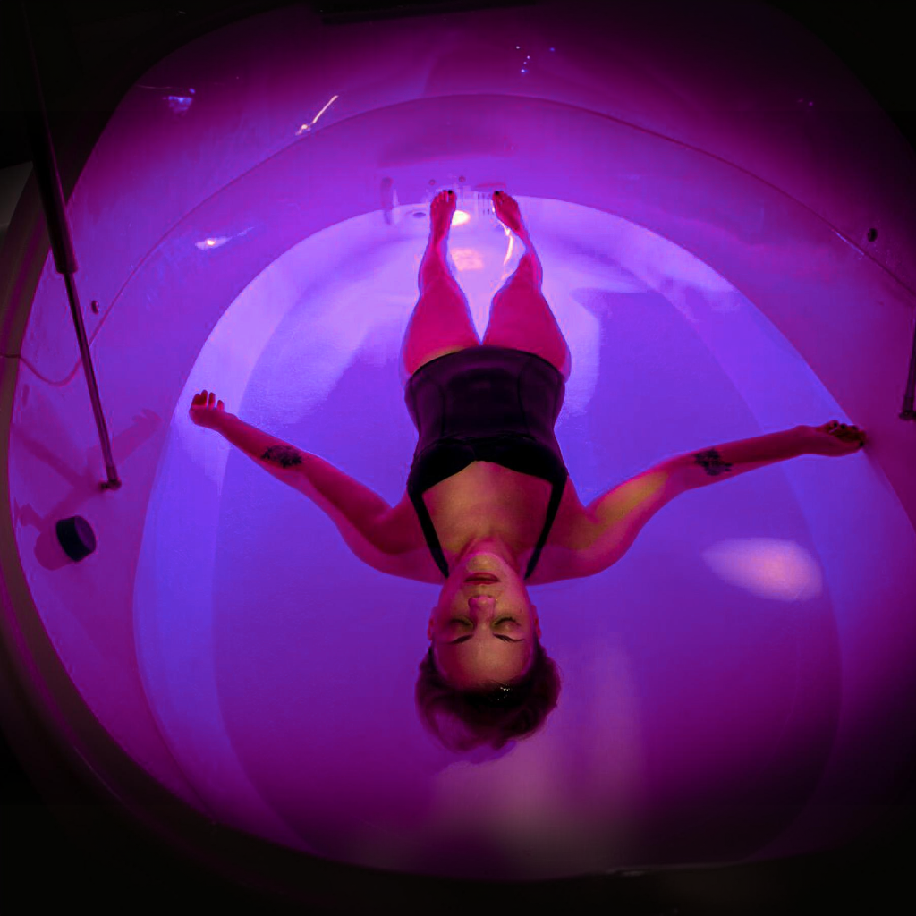 Top-down view of a person floating inside a sealed float tank, showing controlled internal lighting and enclosed architectural design