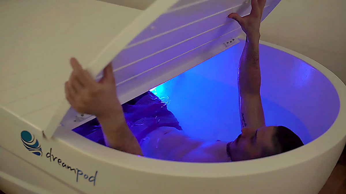 Dreampod Home Float Pro float tank user opening lid with blue illuminated interior in low-light environment