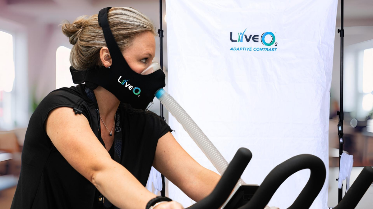 LiveO2 Adaptive Contrast EWOT system with extra-large high altitude chamber and female athlete using oxygen mask during exercise bike training 