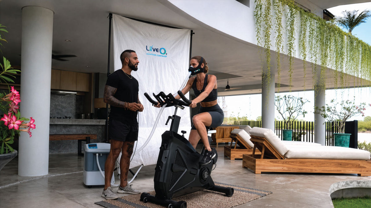 LiveO2 Adaptive Contrast EWOT system with extra-large high altitude chamber and athlete using oxygen mask on an exercise bike in a covered outdoor patio setting