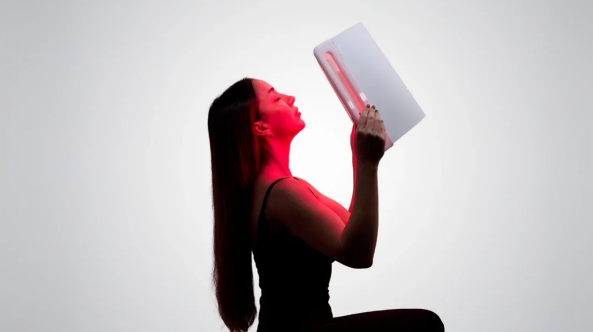 Lumara Illuminate V2 red light therapy panel used for facial treatment in handheld position