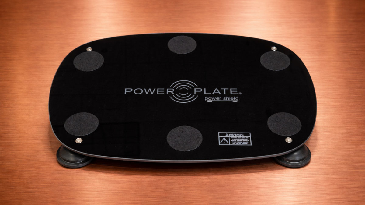 Personal Power Plate Power Shield vibration isolation platform positioned on wood flooring showing the low-profile base used beneath the Personal Power Plate vibration trainer to help reduce vibration transfer through floors during training.