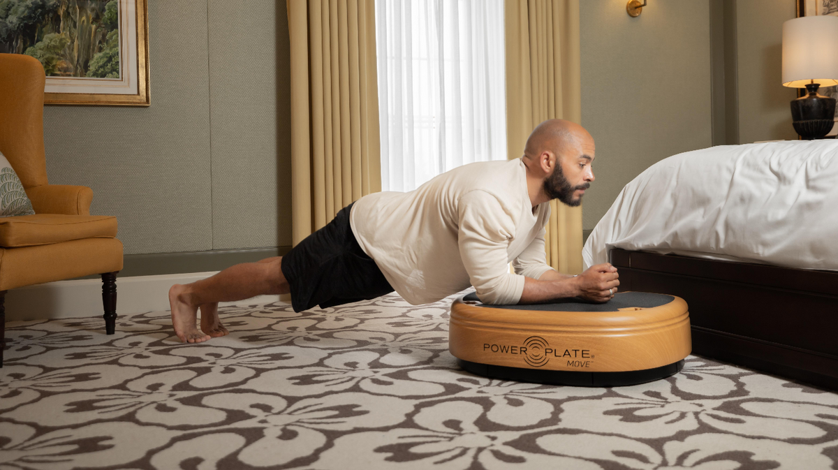 Power Plate MOVE whole body vibration platform used for forearm plank exercise in residential bedroom setting