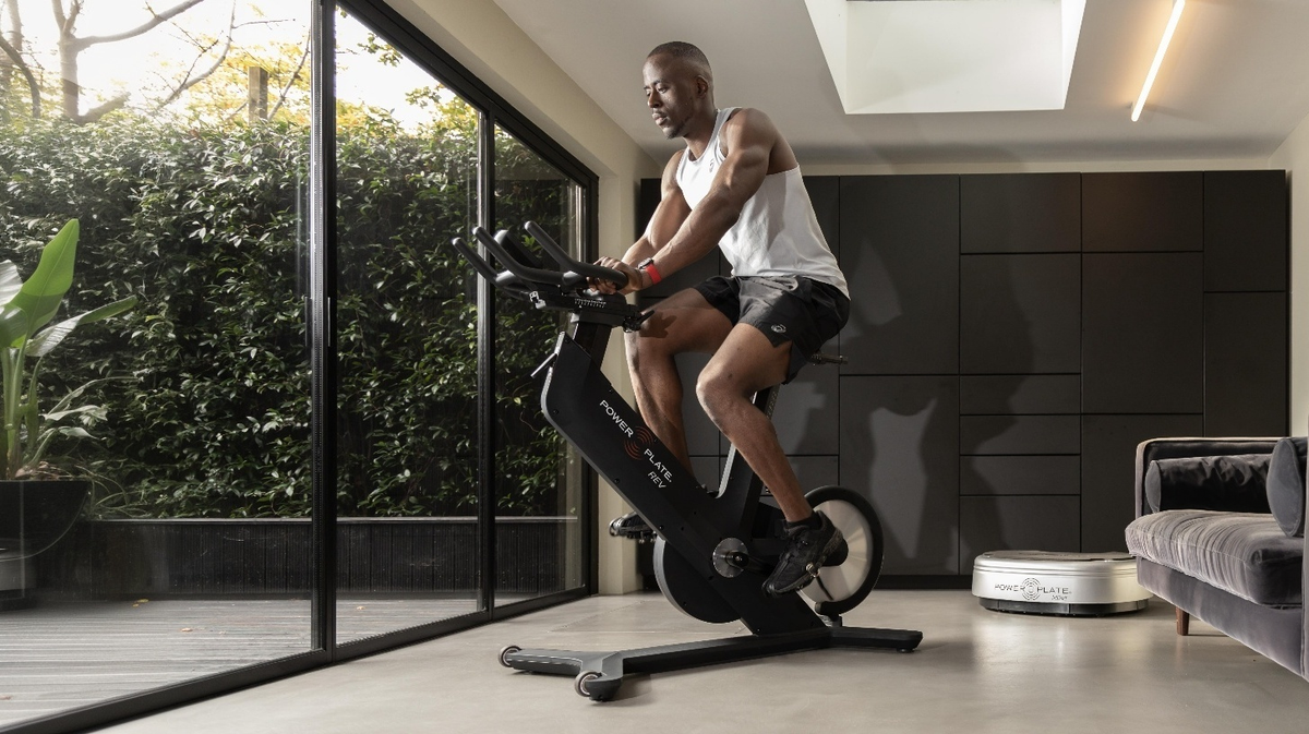 Athlete riding Power Plate REV bike vibration indoor cycle during home fitness workout session