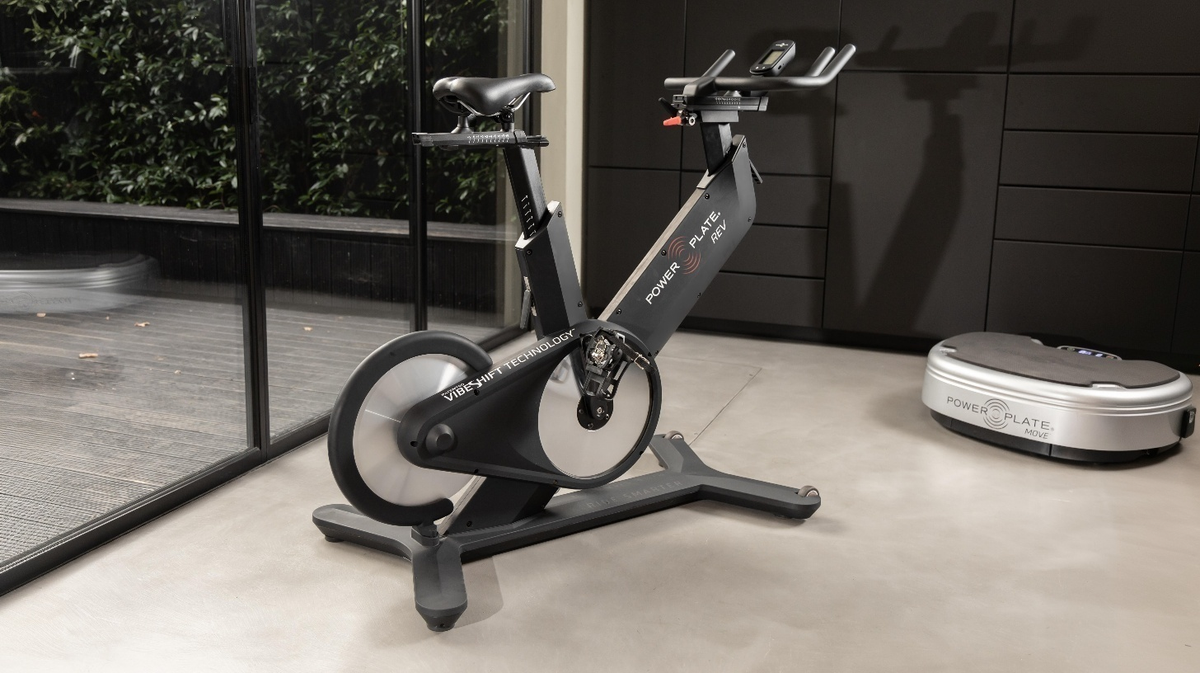 Power Plate REV bike vibration indoor cycling bike positioned in a modern home gym training space