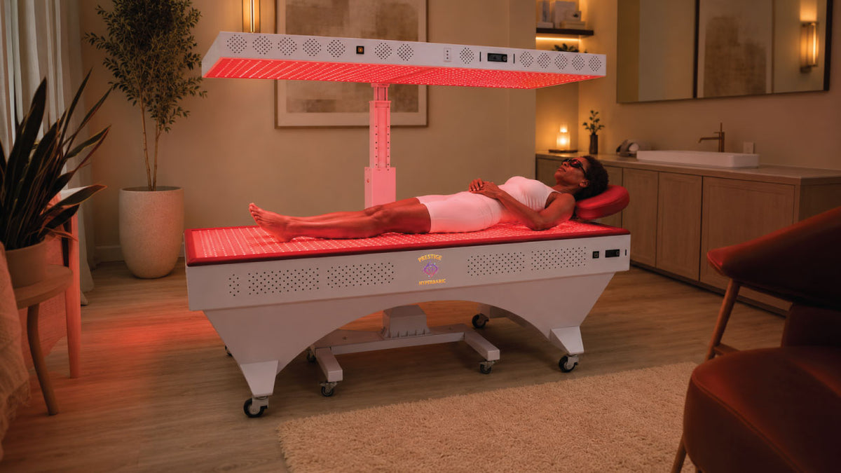 Prestige Pro Modular Red Light Therapy Bed shown during a full-body red light therapy session with user lying between the lower bed panel and raised overhead light panel.